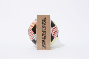 A colorful checkered soccer ball partially obscured by a brown rectangular box with black text that reads, "FOR USE IN ALL SITUATIONS AT ANY TIME AND ANY PLACE," on a white background.