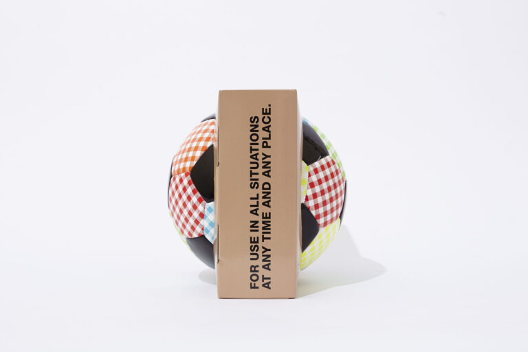 A colorful checkered soccer ball partially obscured by a brown rectangular box with black text that reads, "FOR USE IN ALL SITUATIONS AT ANY TIME AND ANY PLACE," on a white background.