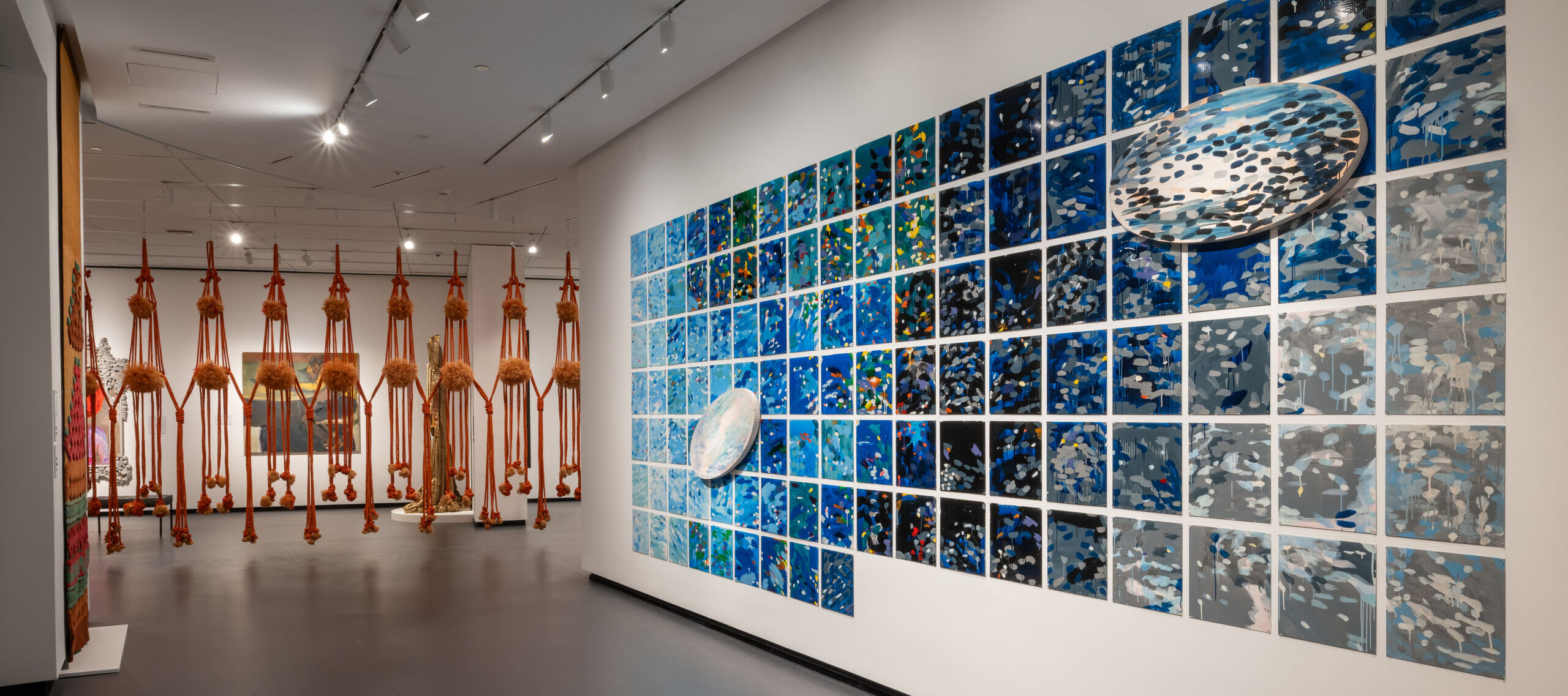 View of an indoor art gallery space with abstract artworks on the walls and sculptures hanging from the ceiling.