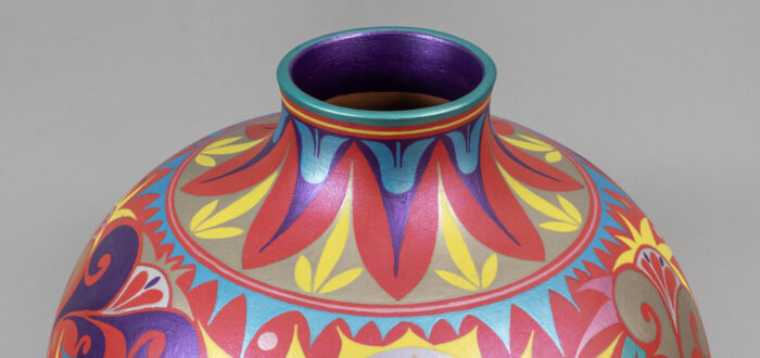 A round ceramic vase with a short neck decorated with intricate geometric and floral patterns painted in red, pink, blue, yellow, and purple.