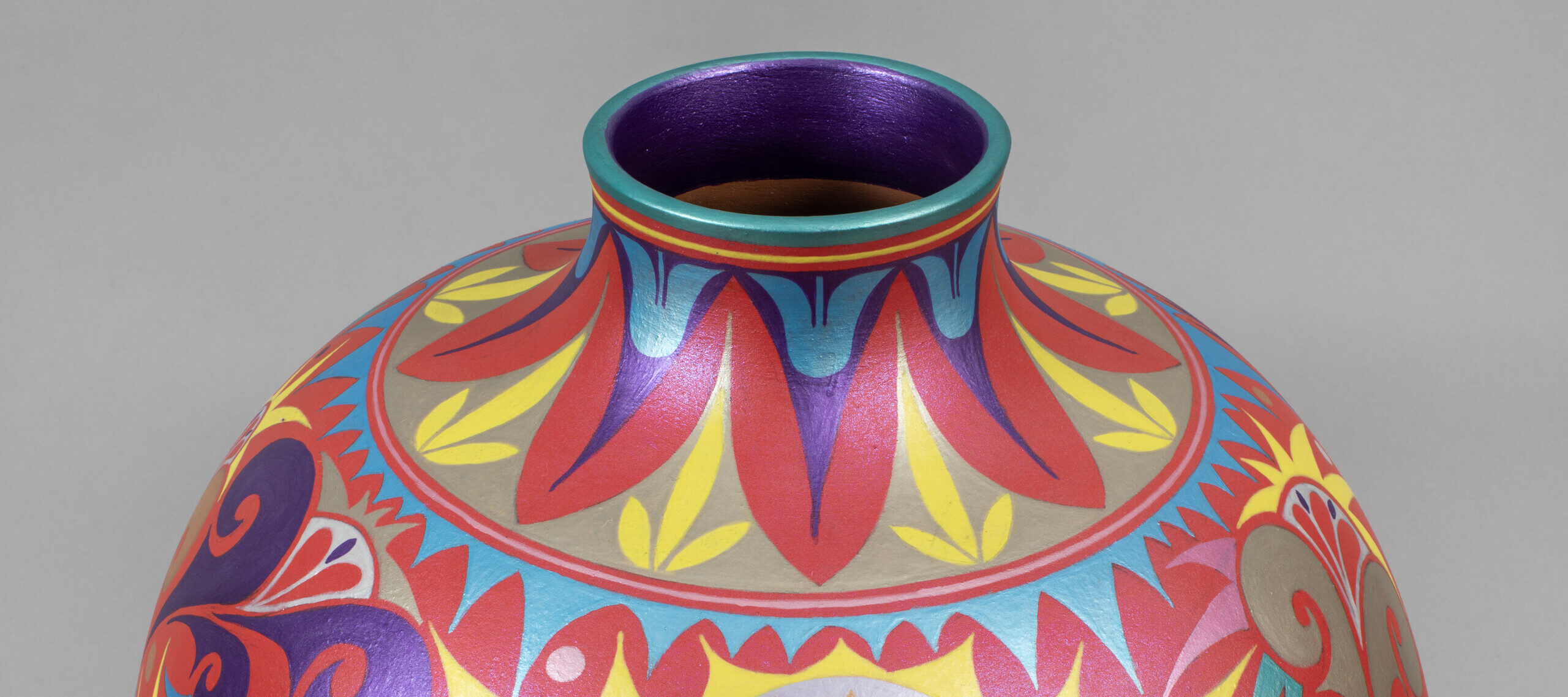 A round ceramic vase with a short neck decorated with intricate geometric and floral patterns painted in red, pink, blue, yellow, and purple.