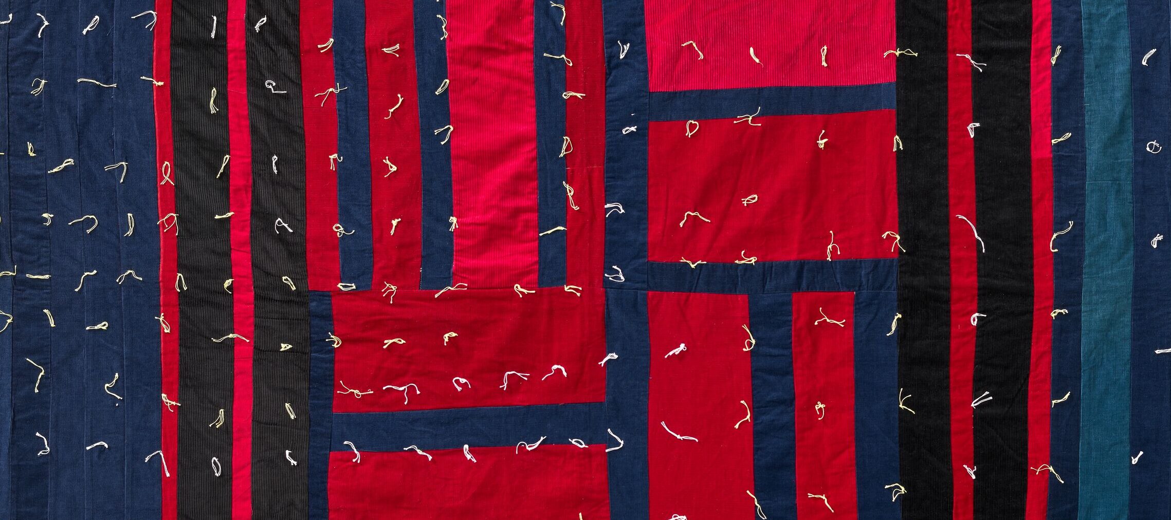 A quilt with a geometric pattern of red and blue rectangles and squares, outlined in black, with visible stitching details throughout.