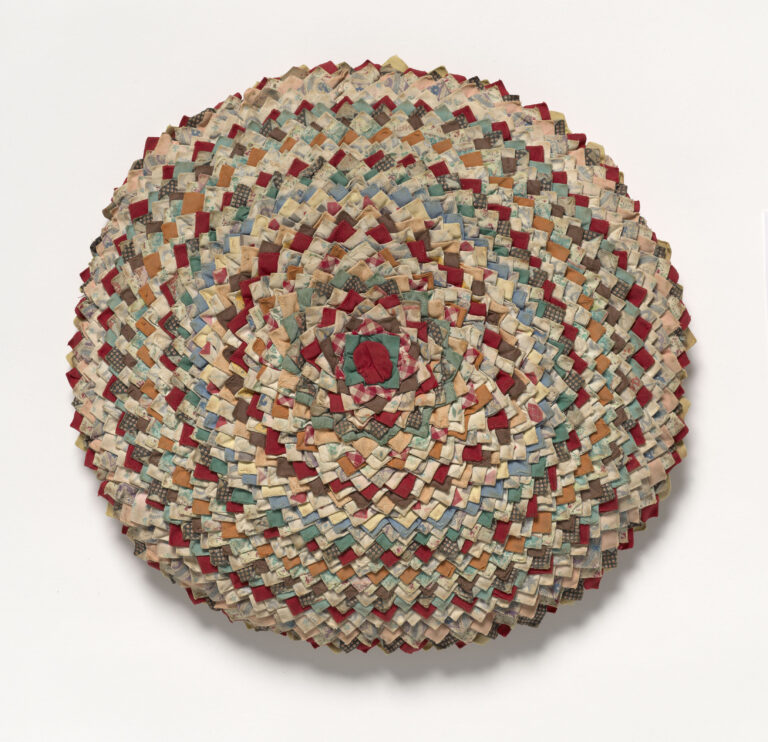 A circular shape created from concentric repeating rows of triangles of fabric in a range of colors, some solid and some with muted patterns.