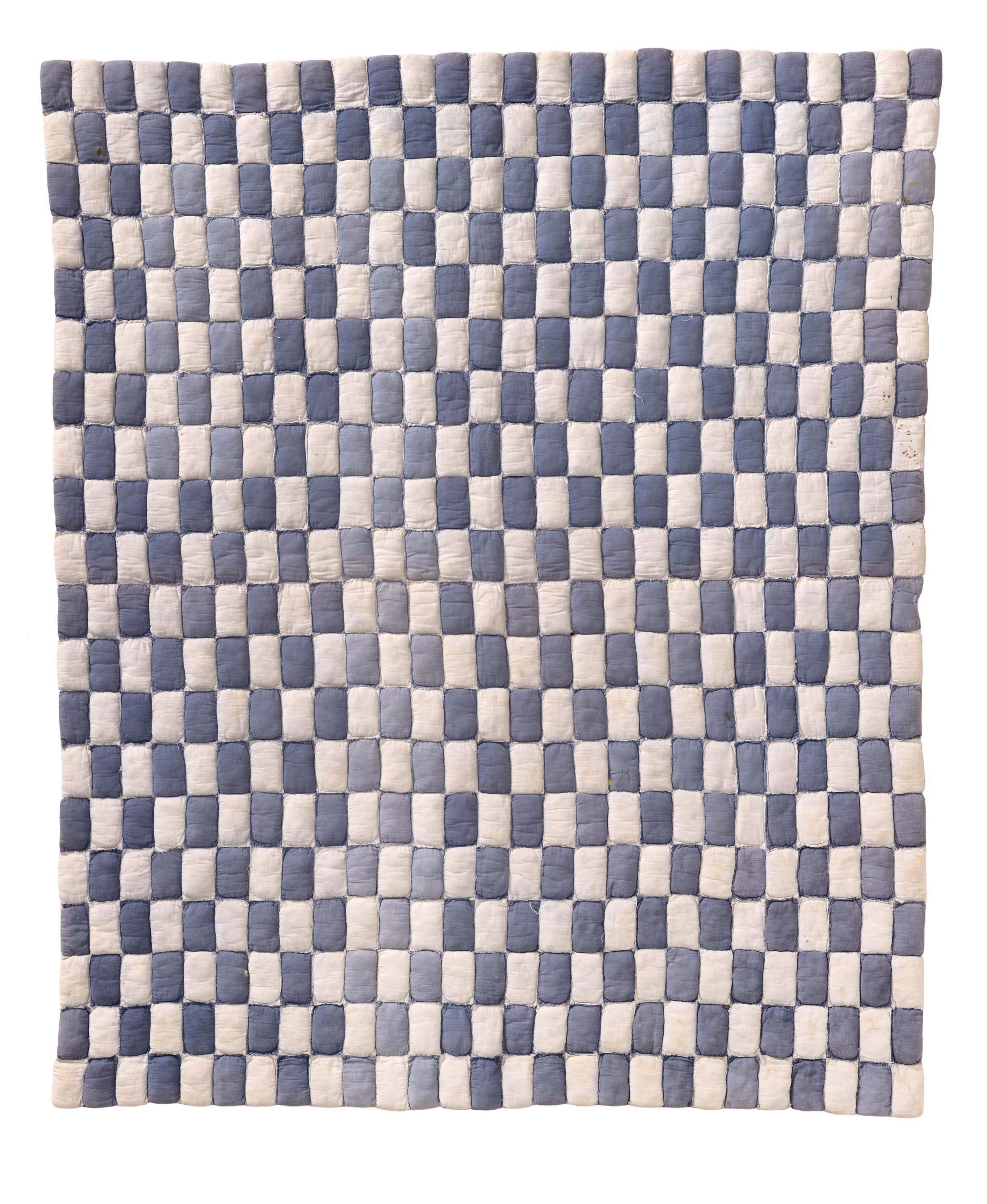 A quilt is composed of numerous small pillow-like cushions stitched together. The tiny rectangular cushions appear in alternating shades of off-white and blue-gray in a checkerboard pattern.